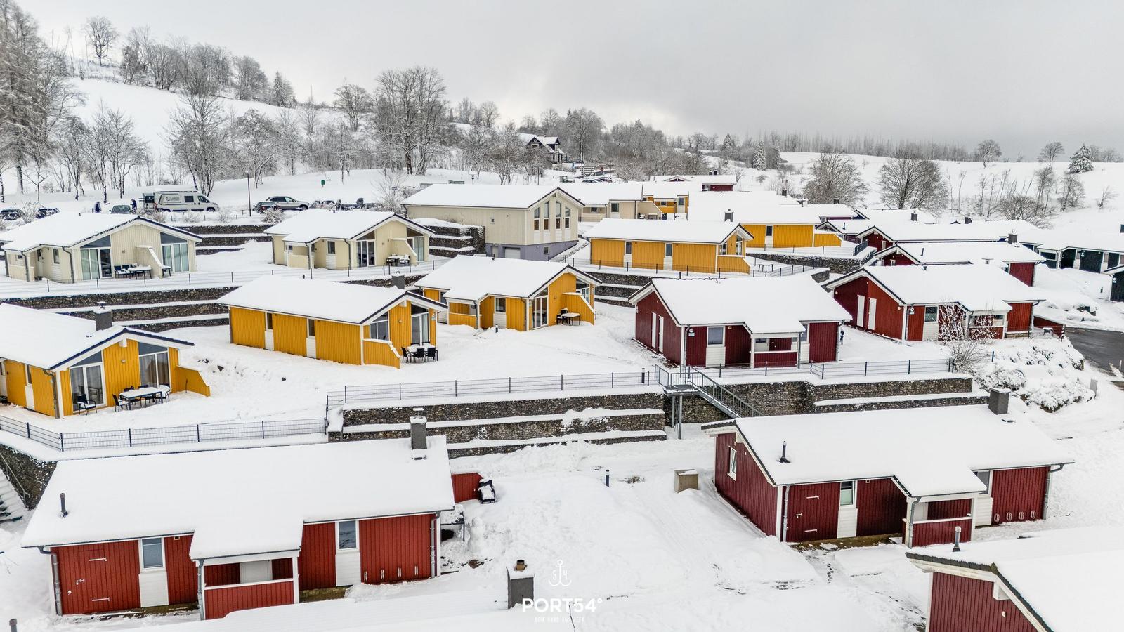 Schneebedeckte Ferienhäuser in bunten Farben auf einer Hanglage.
