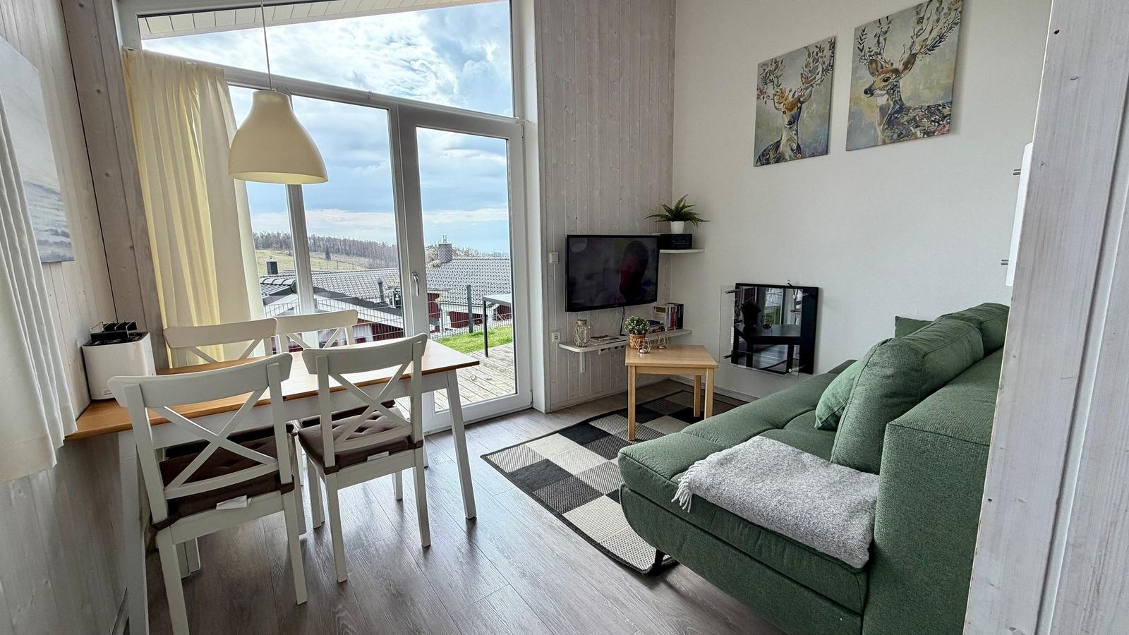 Wohn- und Essbereich mit grünem Sofa, TV und Blick auf die Terrasse.
