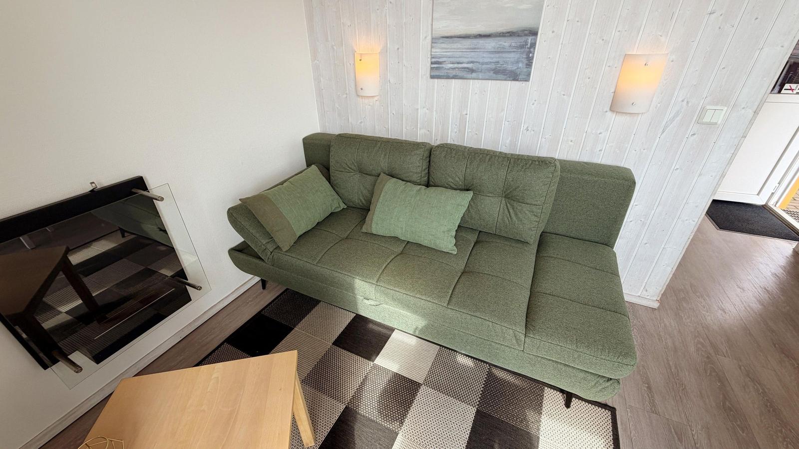 Grünes Sofa mit Kissen, gemusterter Teppich und Wandbeleuchtung im Wohnbereich.