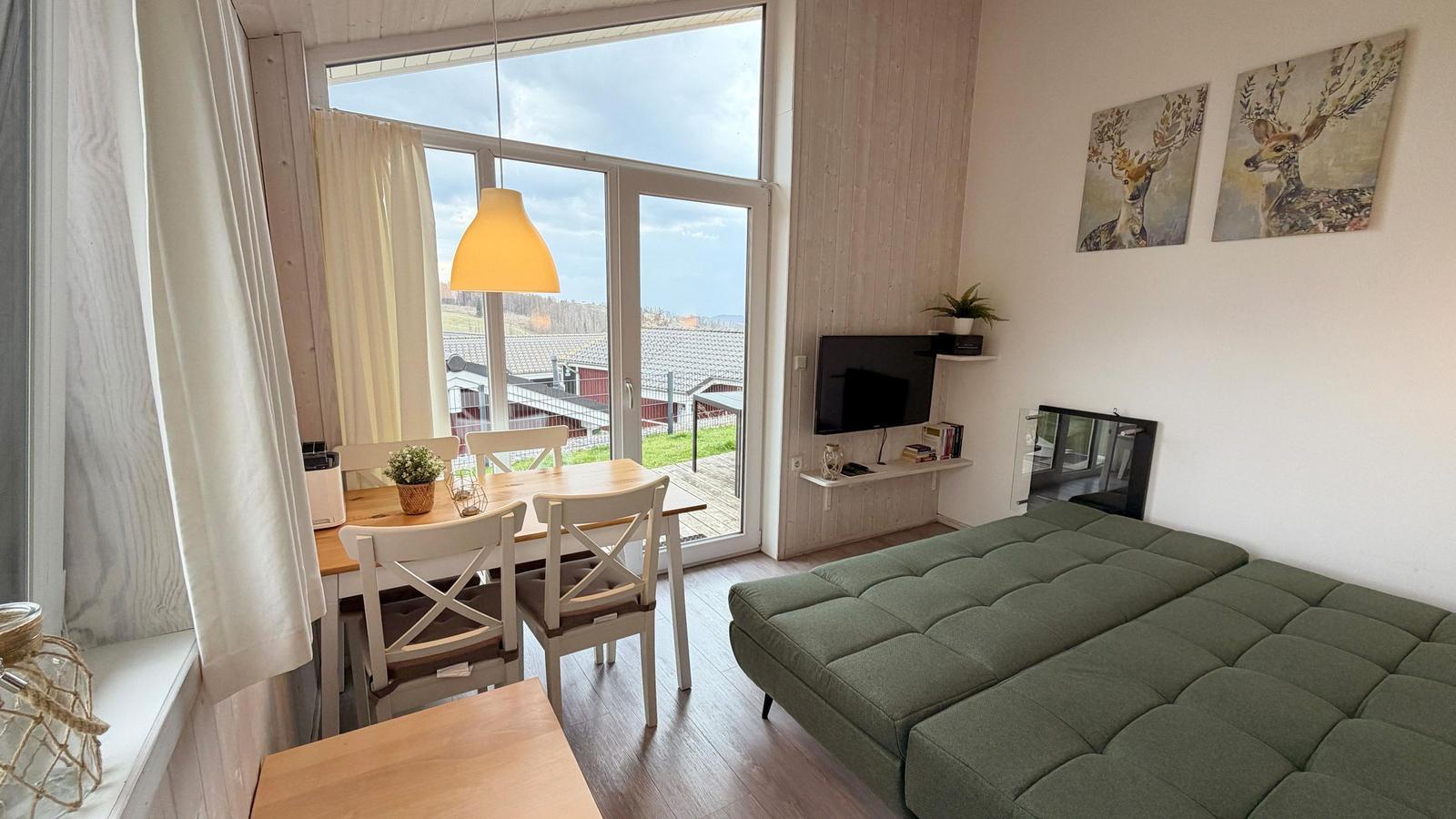 Wohn- und Essbereich mit grünem Sofa, TV und Blick auf die Umgebung.