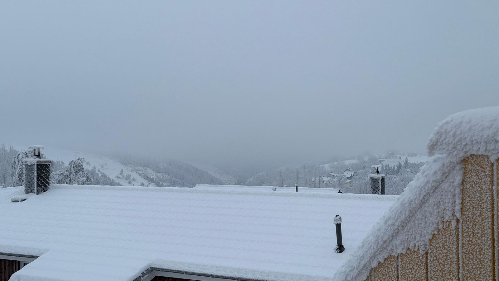 Schneebedeckter Dachfirst mit Blick auf verschneite Berge und Nebel.