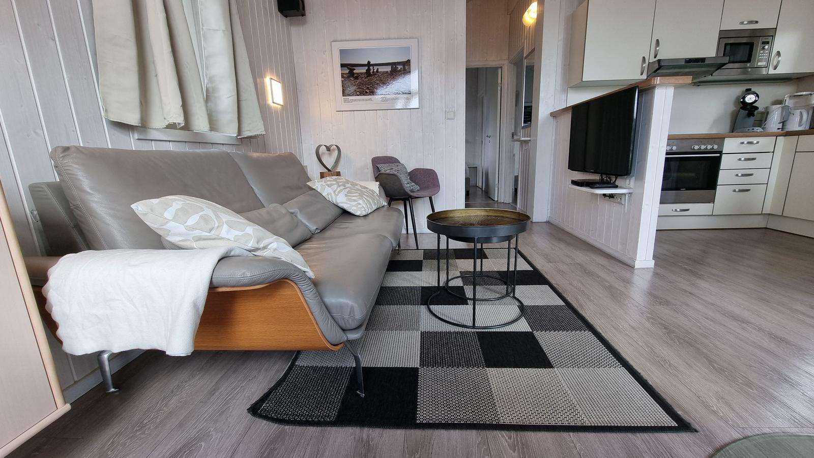 Wohnzimmer mit Sofa, Tisch und Küche im Hintergrund.