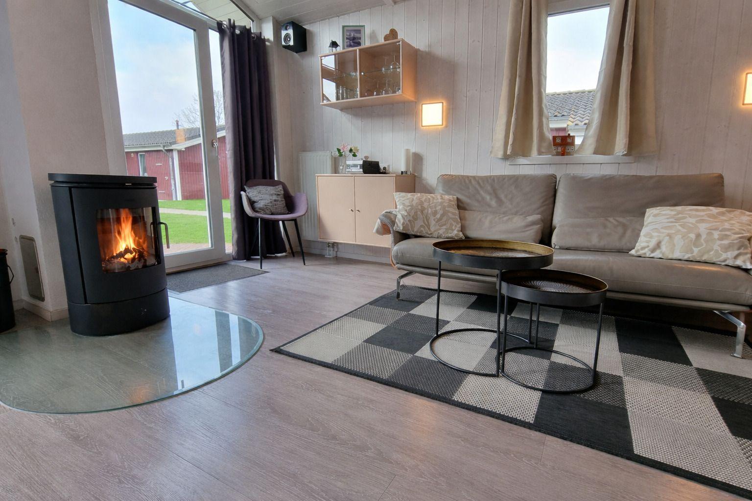 Wohnzimmer mit Kamin, Sofa, Tisch und Fenster. Holzdielen und Teppichboden.