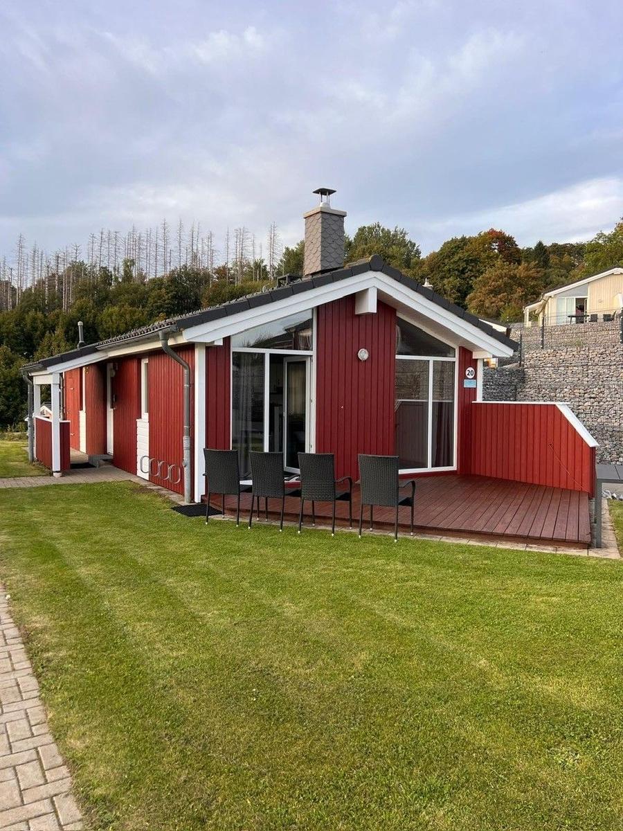 Rotes Ferienhaus mit Terrasse und Garten. Vier Stühle stehen auf der Terrasse.