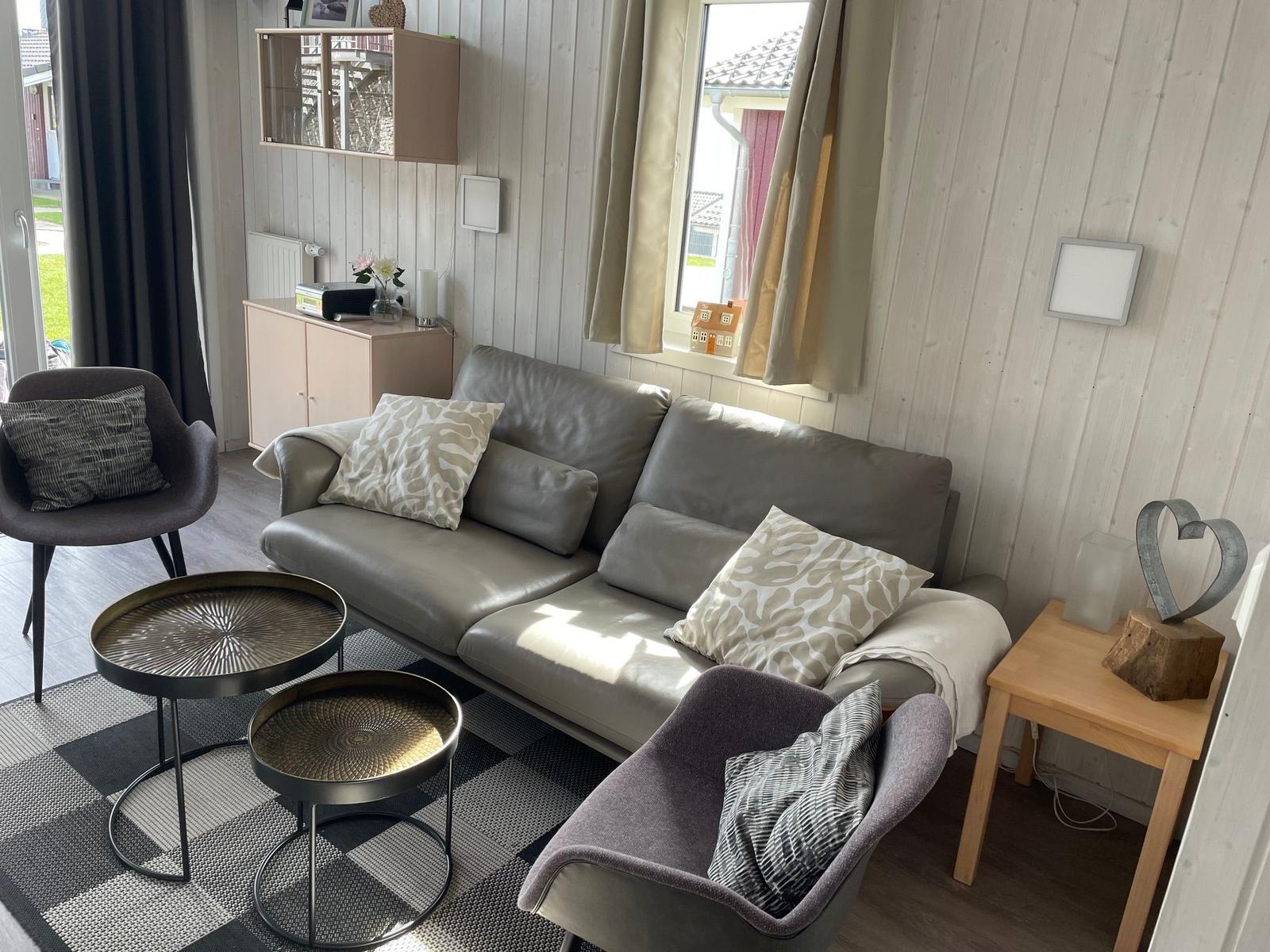 Wohnzimmer mit Sofa, zwei Sesseln und zwei runden Tischen auf gemustertem Teppich.