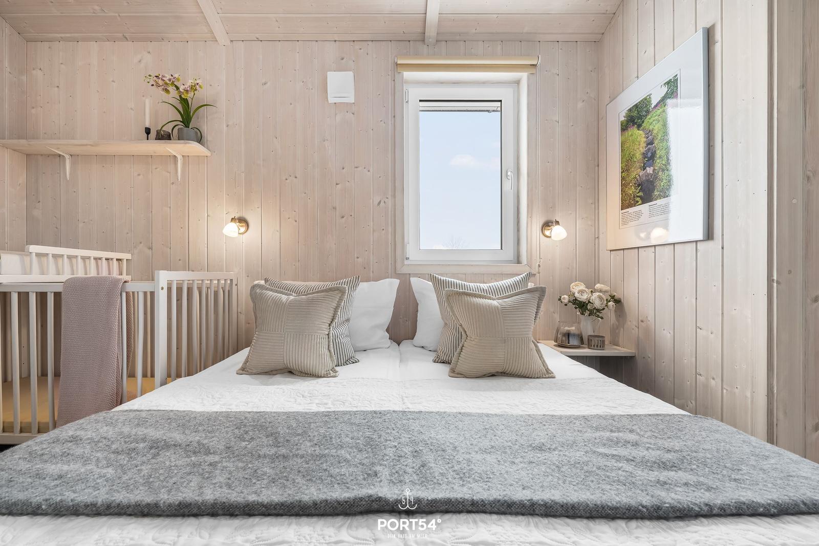 Schlafzimmer mit Bett, Kinderbett und Fenster. Holzwände und Bilder an der Wand.