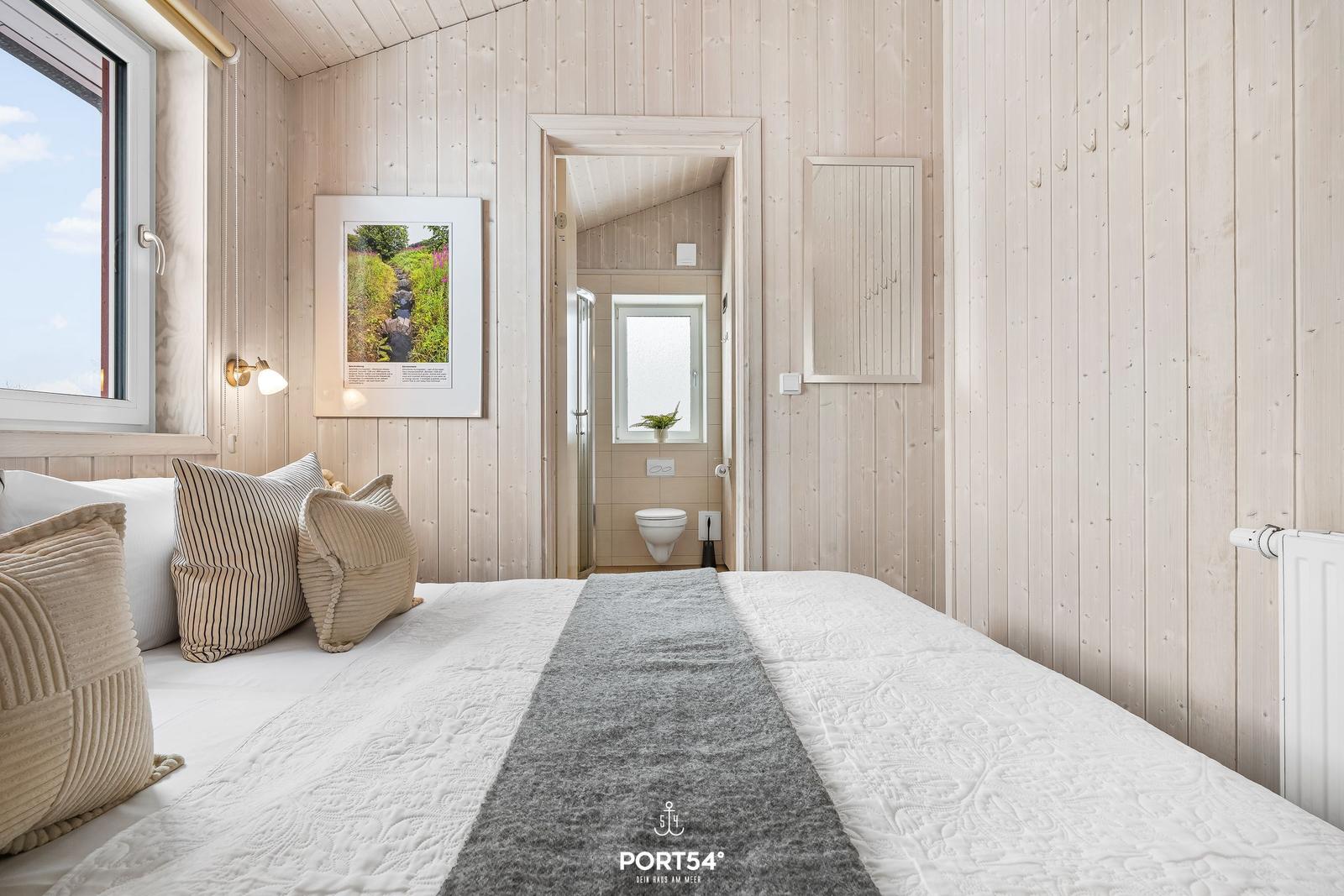 Schlafzimmer mit Holzwand, Bett und Blick in das Badezimmer.