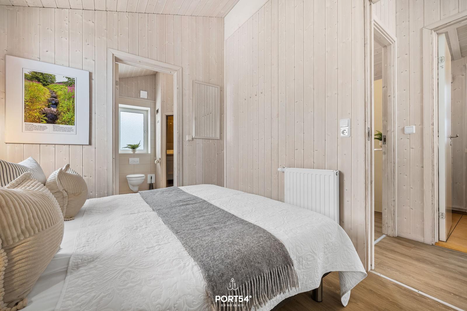Schlafzimmer mit Holzwand, Bett und Blick in Badezimmer und Flur.