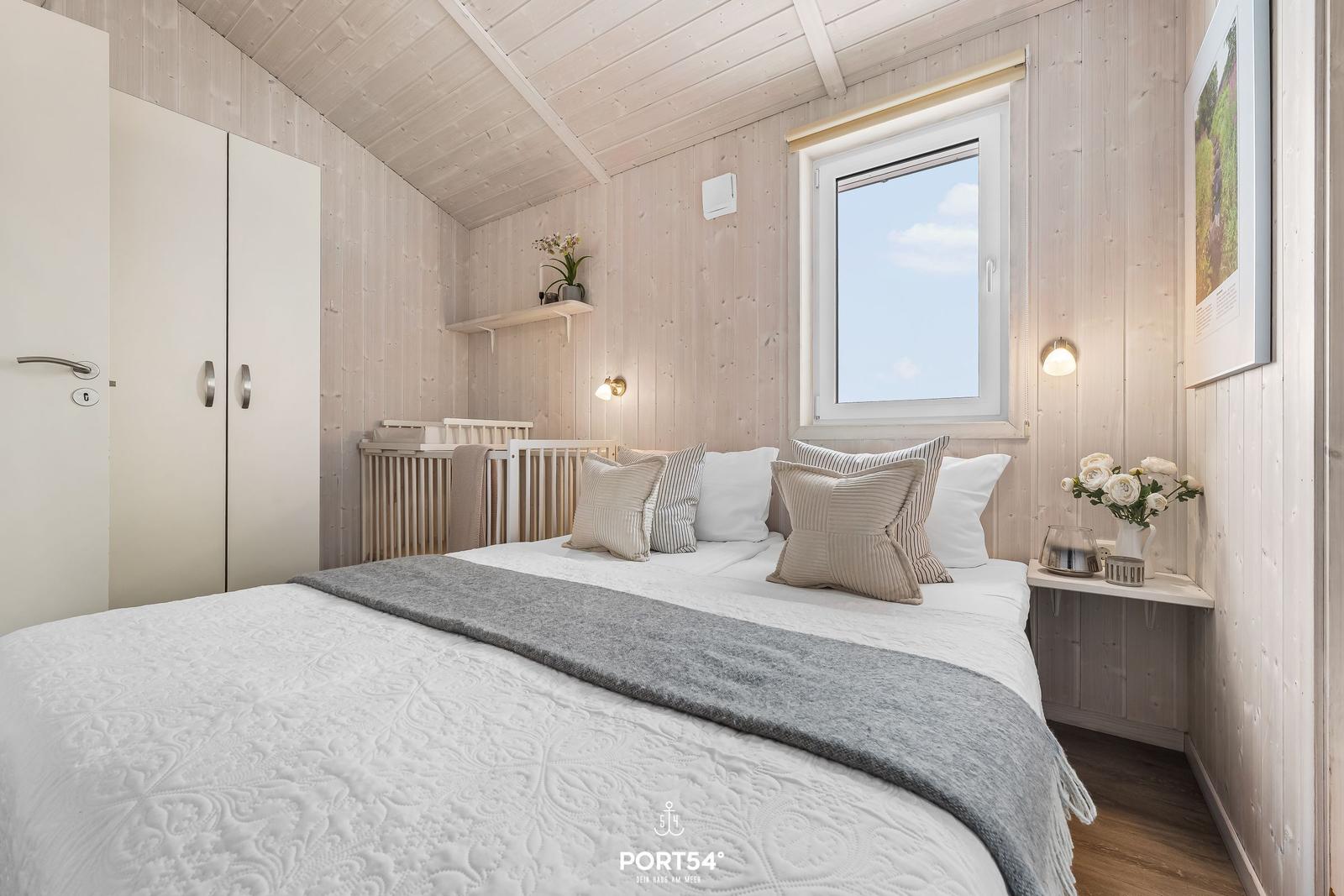 Schlafzimmer mit Bett, Kleiderschrank und Fenster. Holzwand und Dachschrägen.
