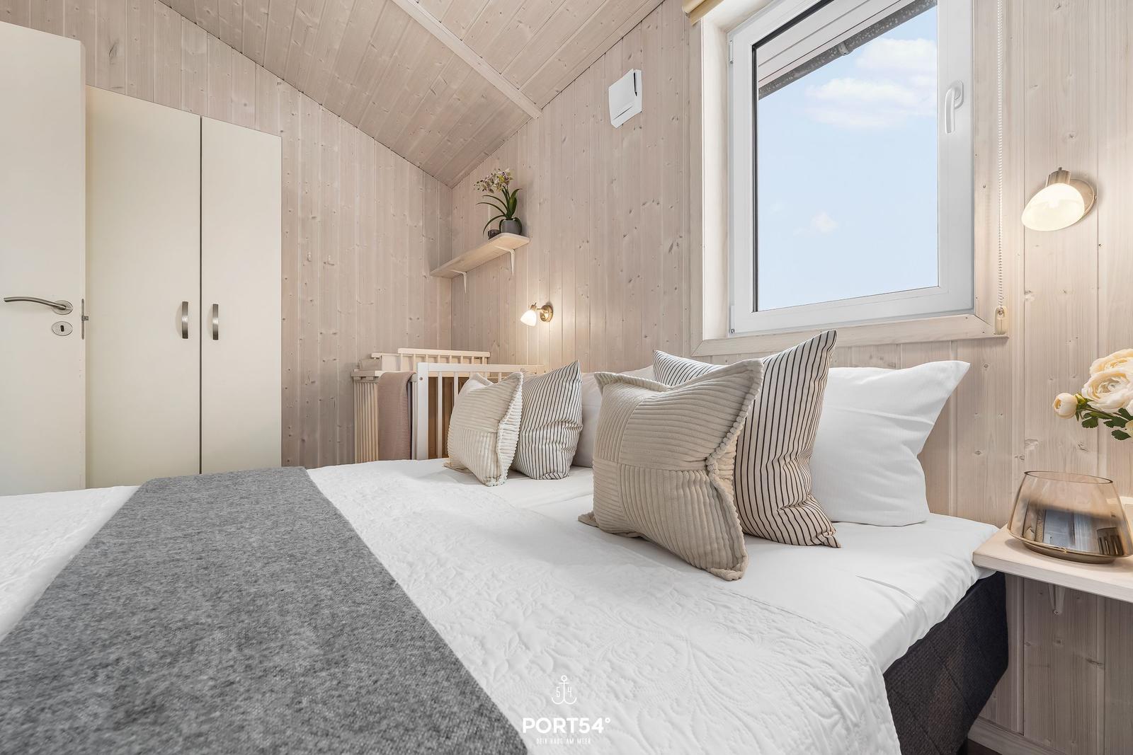 Schlafzimmer mit Holzwand, Bett, Fenster und Kleiderschrank.