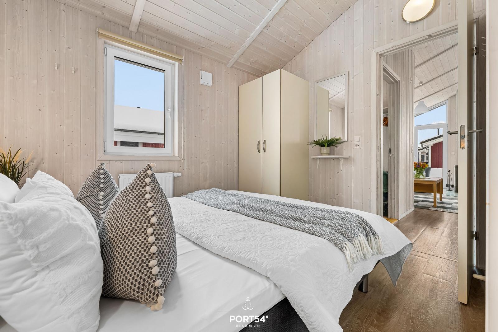 Schlafzimmer mit Bett, Kleiderschrank und Fenster. Holzwand und Boden.