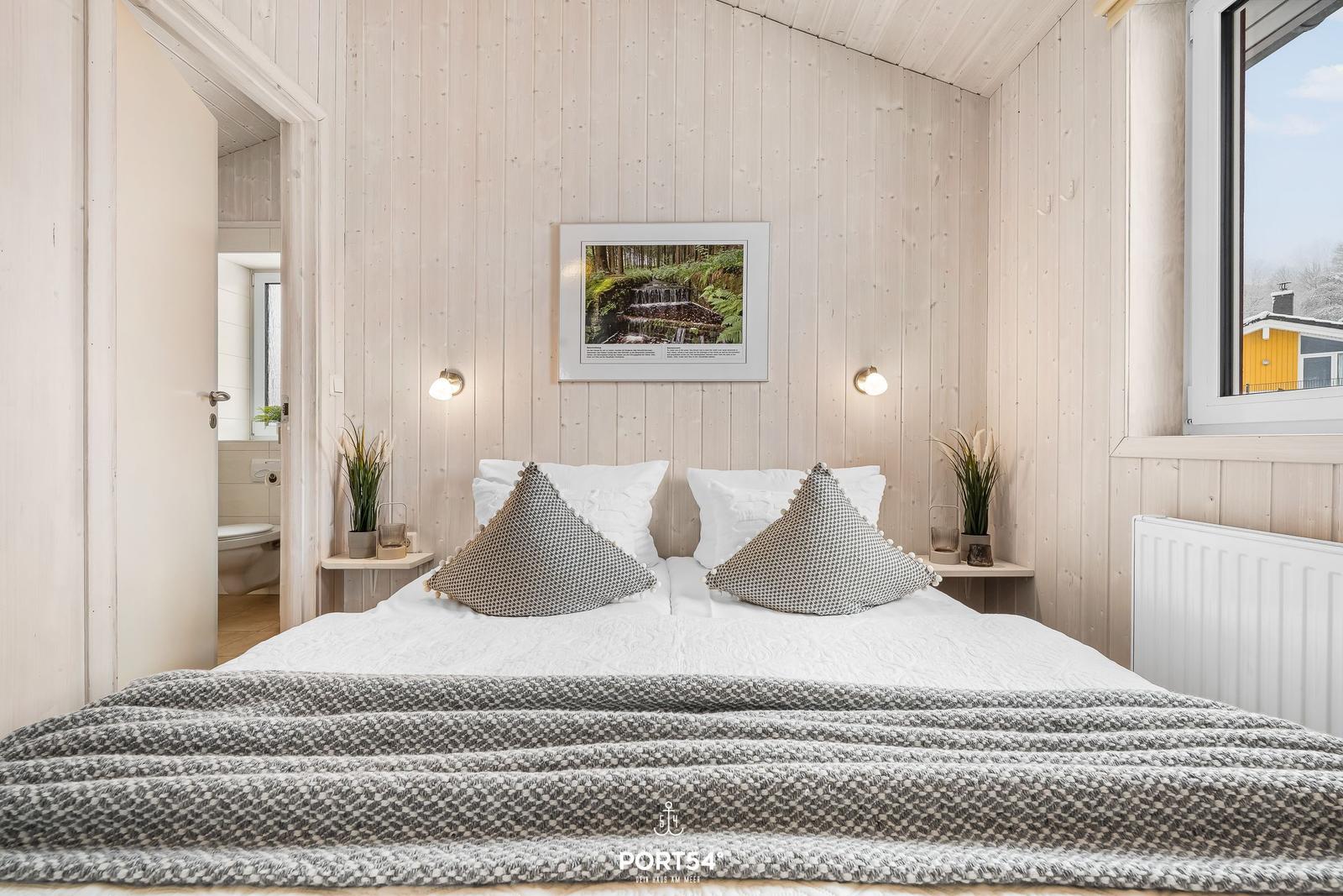 Schlafzimmer mit Bett, Wandbild und Fenster. Durchgang zur Toilette.