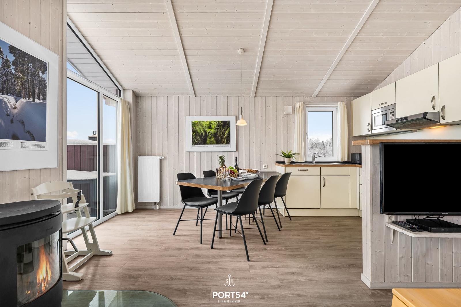 Wohnküche mit Esstisch, Kamin und großem Fenster. Moderne Einrichtung und hellen Holzwand.