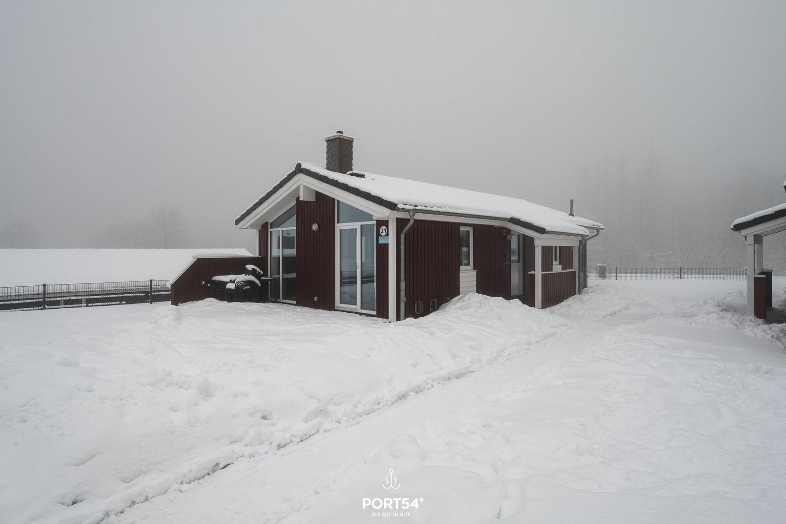 Ein rotes Ferienhaus mit Schnee bedeckt, großes Fenster und Terrasse.