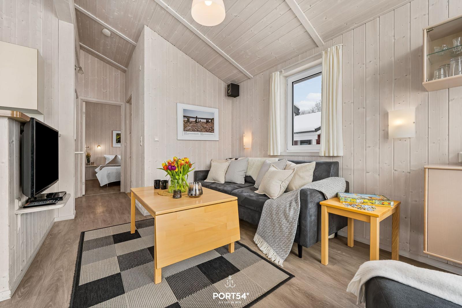 Wohnzimmer mit Sofa, Tisch und TV. Durchgang zur Schlafzimmer.