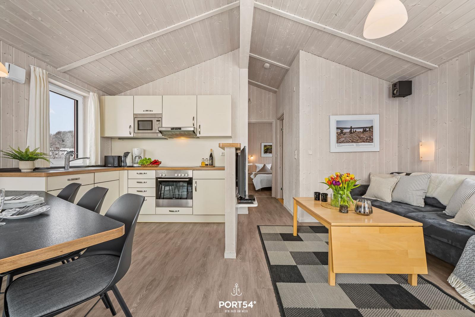 Küche, Essbereich und Wohnzimmer in einem Ferienhaus mit Holzwand und -decke.