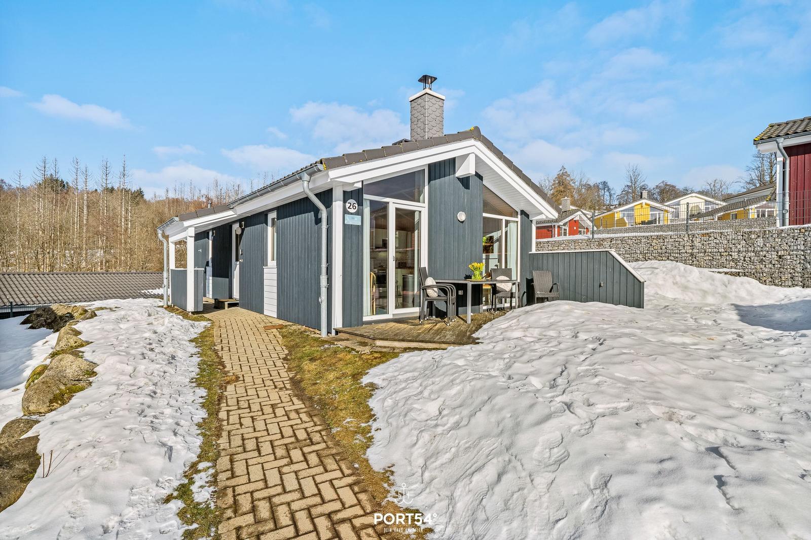 Moderne Ferienhaus mit Terrasse, Schnee und Holzweg. Glastüren und graue Fassade.