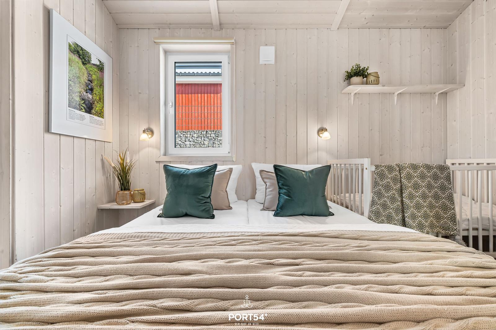 Schlafzimmer mit Bett, Krippe und Fenster mit Blick auf rote Wand.