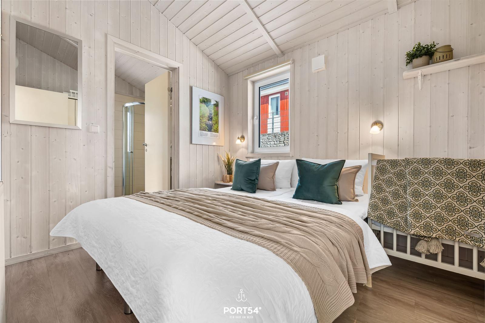 Schlafzimmer mit Bett, Fenster und angrenzender Dusche.