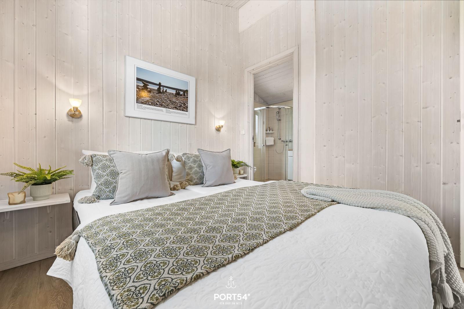 Schlafzimmer mit Bett, Wandbild und angrenzender Dusche.