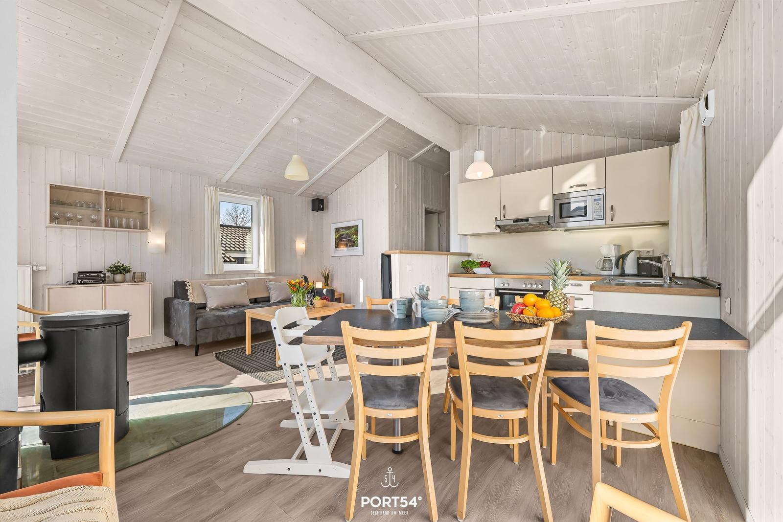 Wohnküche mit Esstisch, Sofa und Kaminofen. Weiße Holzwände und Decke.