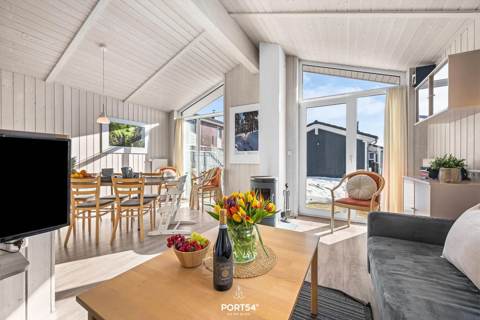 Wohn- und Essbereich mit Holzdecke, Sofa, Tisch und Blick auf den Außenbereich.