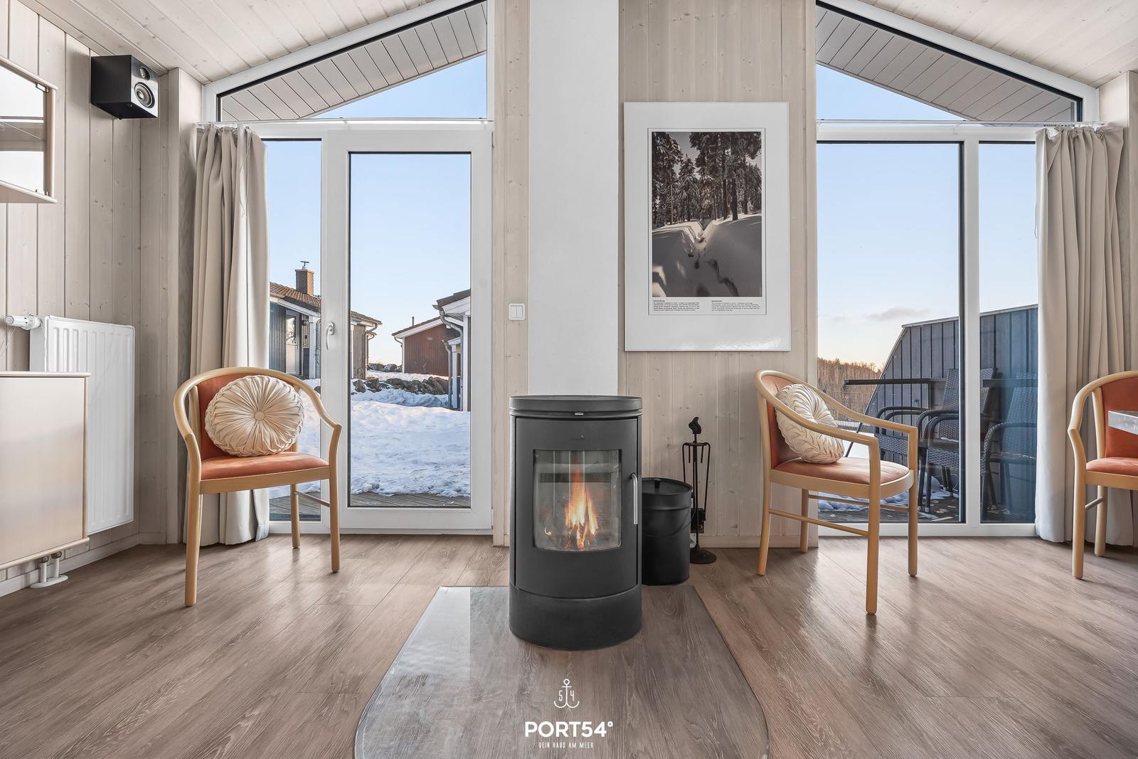 Raum mit Kamin, zwei Stühlen und Blick auf Schnee und Balkon.
