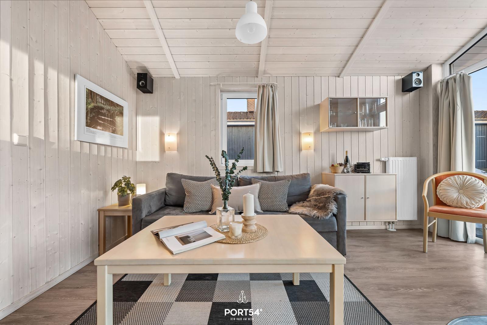 Wohnzimmer mit Sofa, Tisch und Stuhl. Holzwände und Decke. Fenster mit Vorhang.