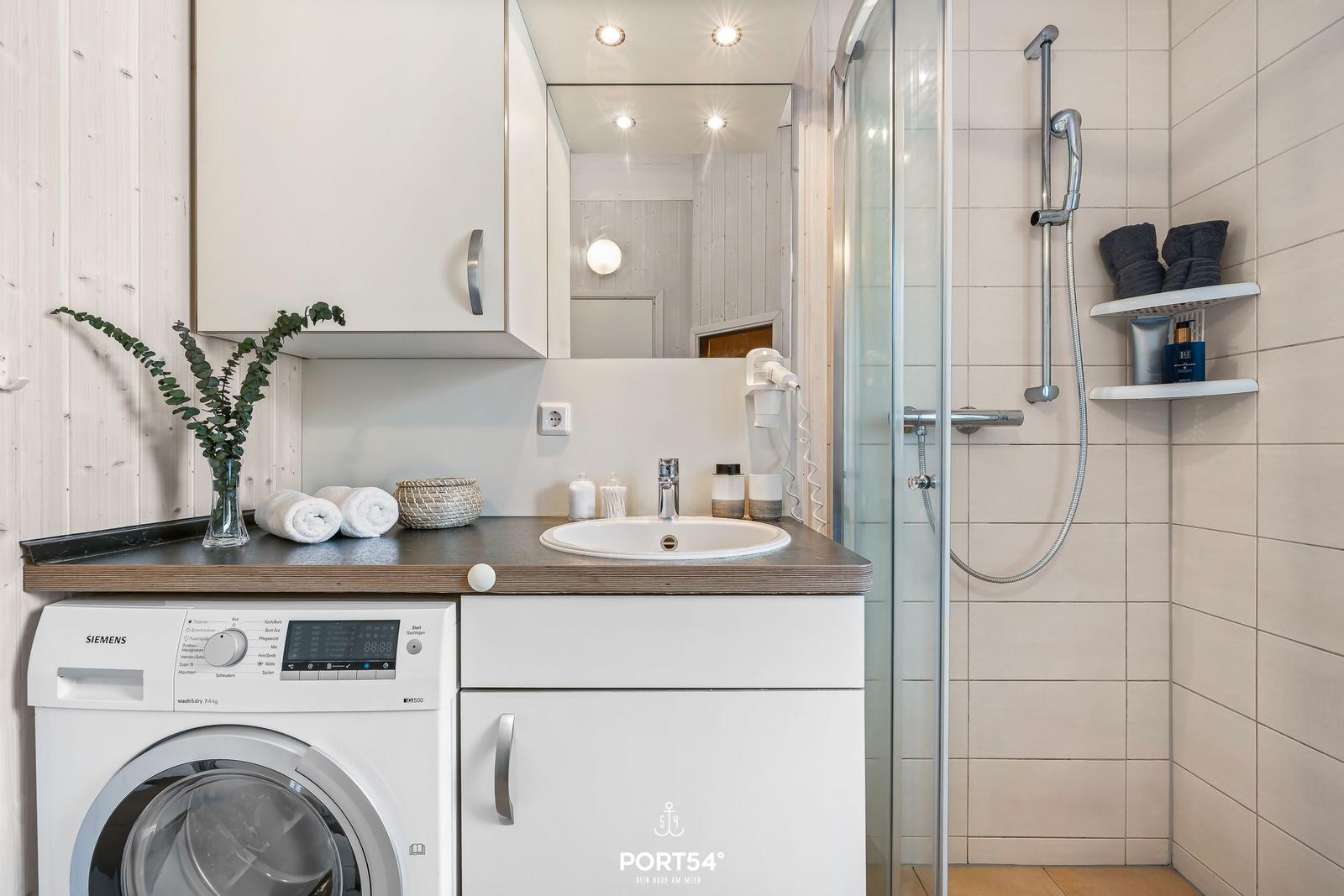Badezimmer mit Dusche, Waschmaschine und Spiegel