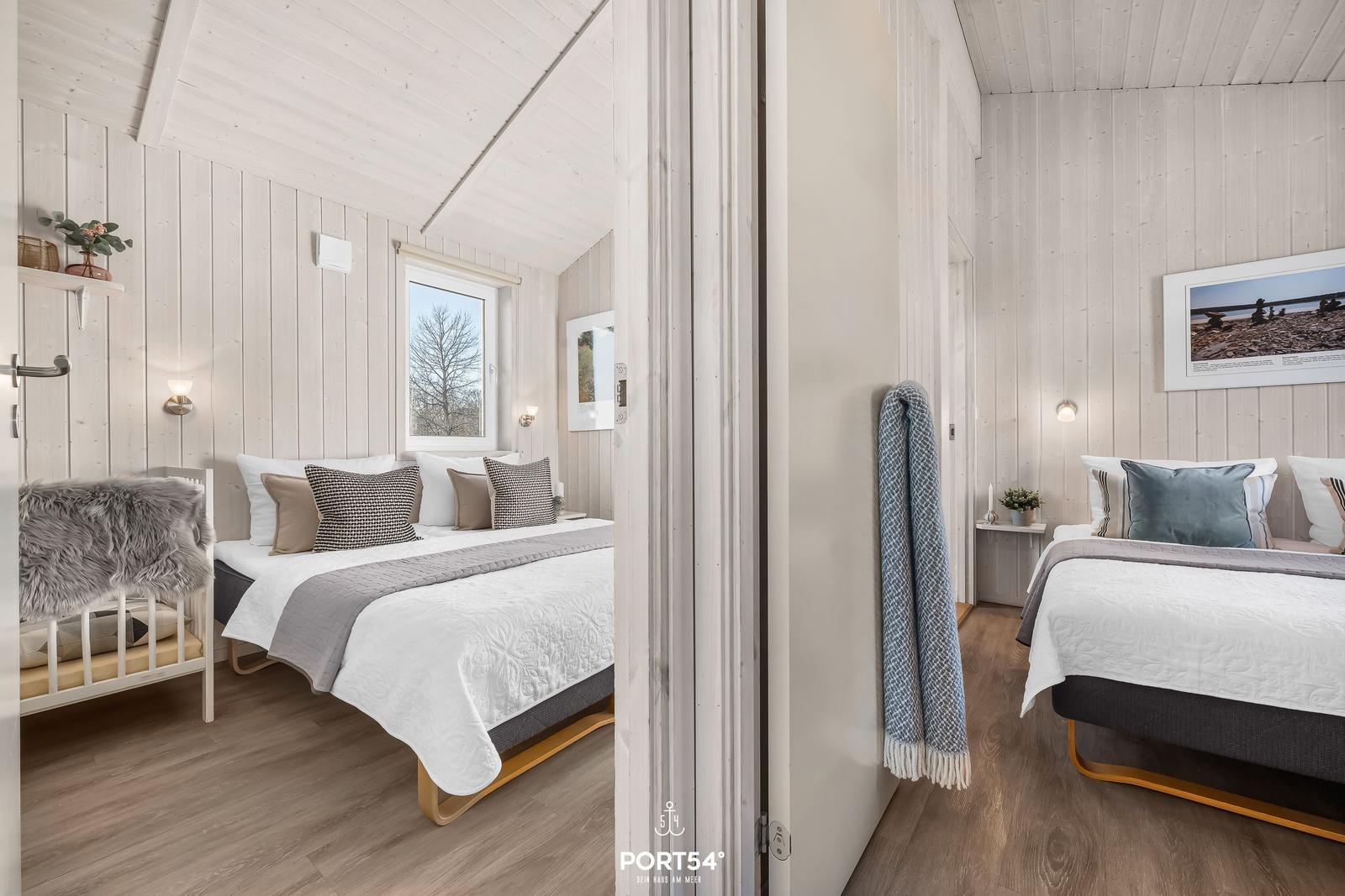 Zwei Schlafzimmer mit Betten, Holzwänden und Fenstern. Ein Raum hat eine Wiege.
