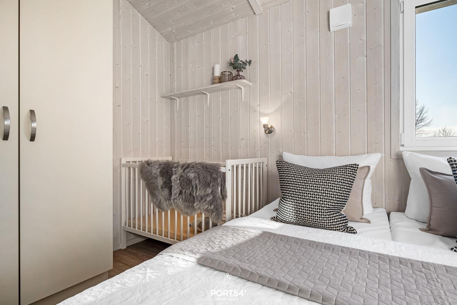 Schlafzimmer mit Bett, Kinderbett und Kleiderschrank. Holzwände und Fenster.