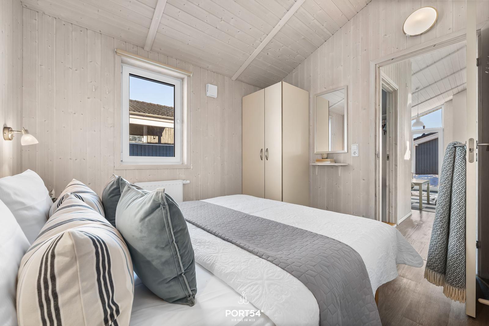 Schlafzimmer mit Bett, Kleiderschrank und Fenster. Blick auf Außenbereich.