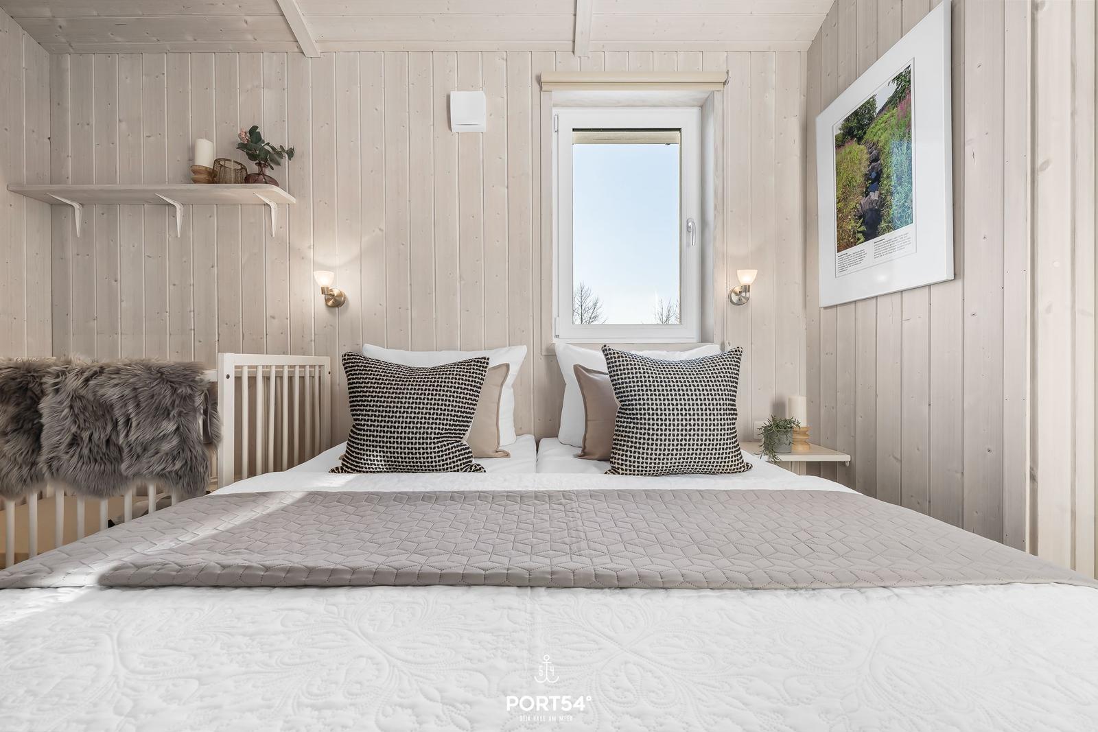 Schlafzimmer mit Bett, Fenster und Wandbild. Holzwände und dekorative Kissen.