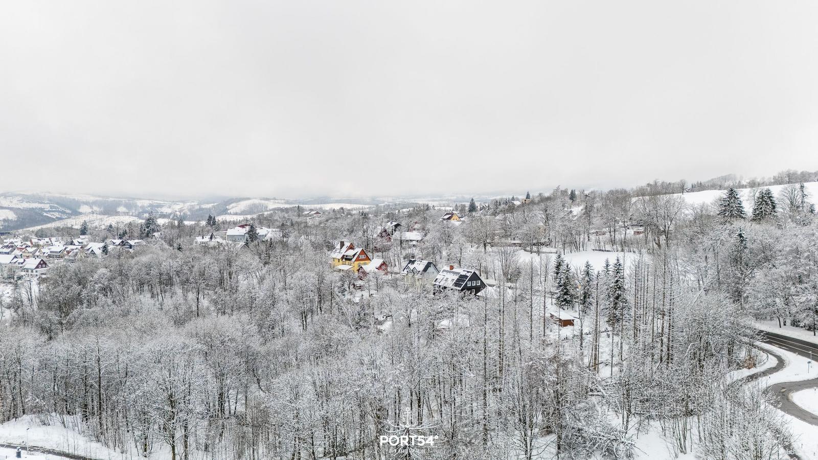 Schneebedeckte Landschaft mit Häusern und Wäldern in einer Bergregion.