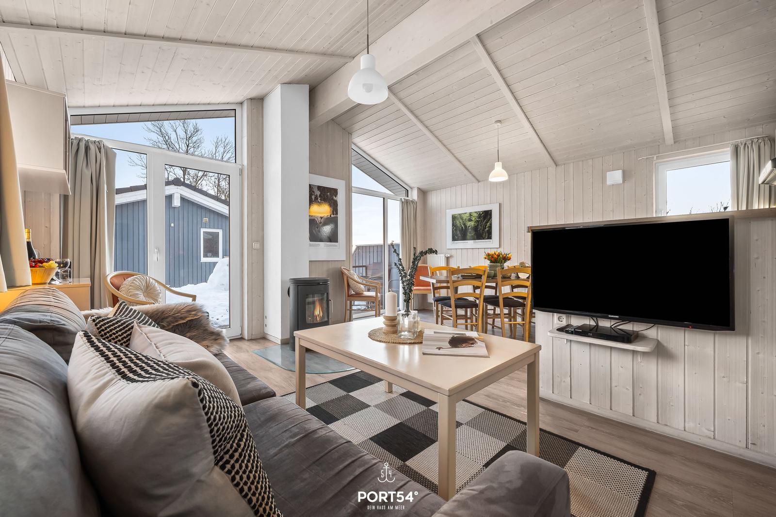 Wohnzimmer mit Sofa, Esstisch und TV. Holzwände und große Fenster.
