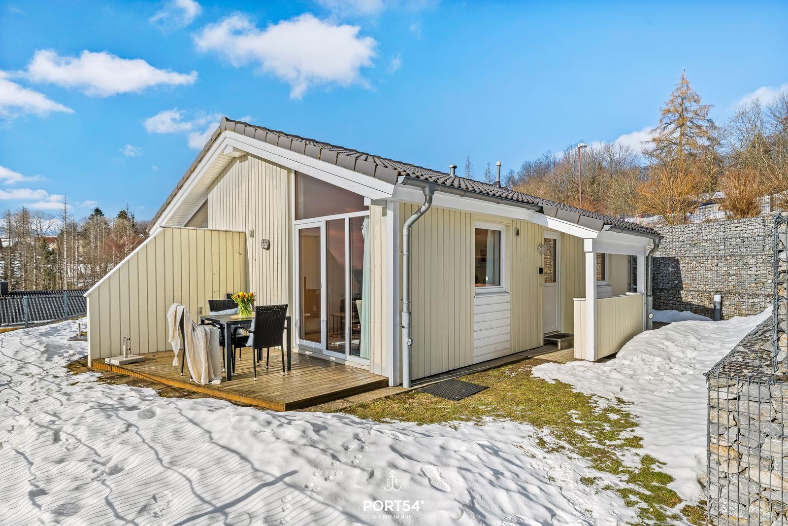 Wohnhaus mit Terrasse, Tisch und Stühlen. Schnee bedeckt den Boden.