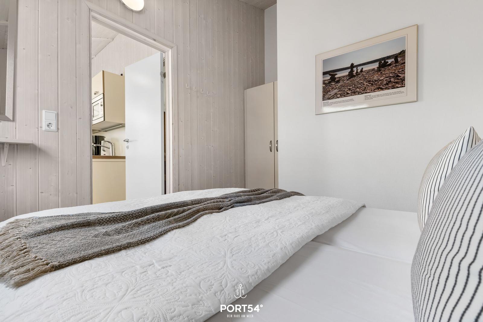 Schlafzimmer mit Bett, Wandbild und Blick in die Küche.
