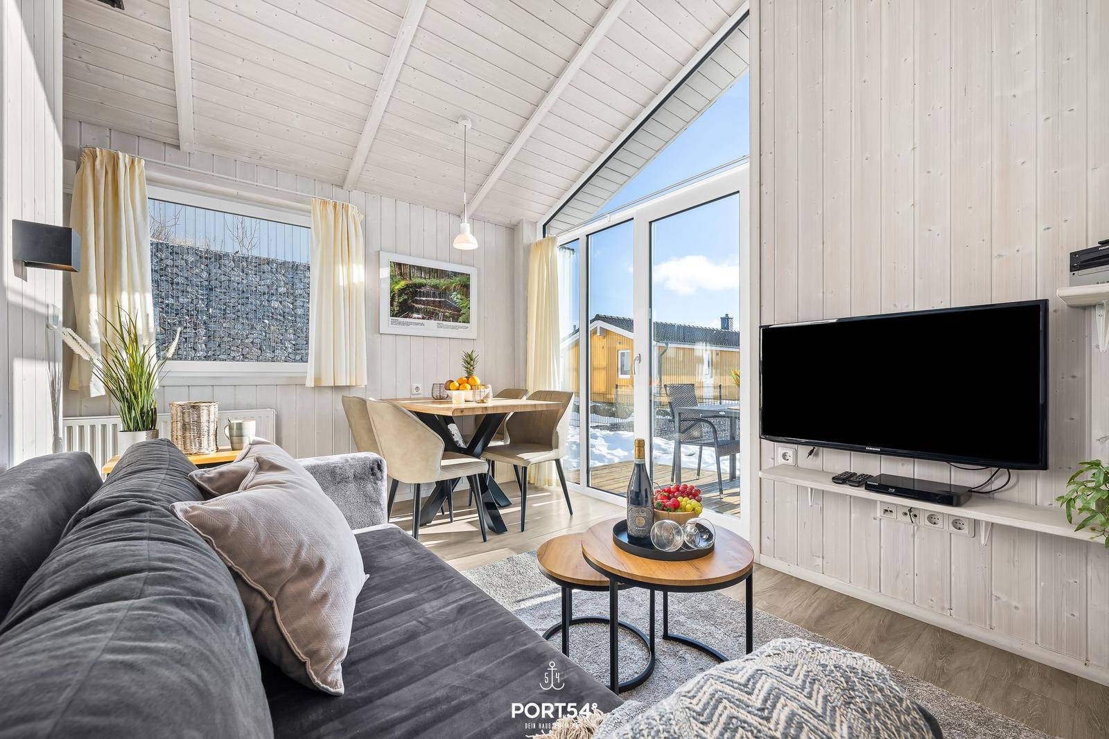 Wohn- und Essbereich mit TV, Tisch, Stühlen und Blick auf Balkon.