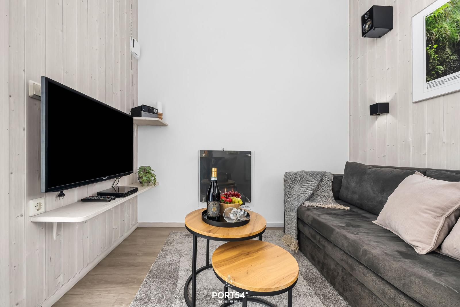 Wohnzimmer mit Sofa, Fernseher und kleinem Tisch mit Obst und Wein.