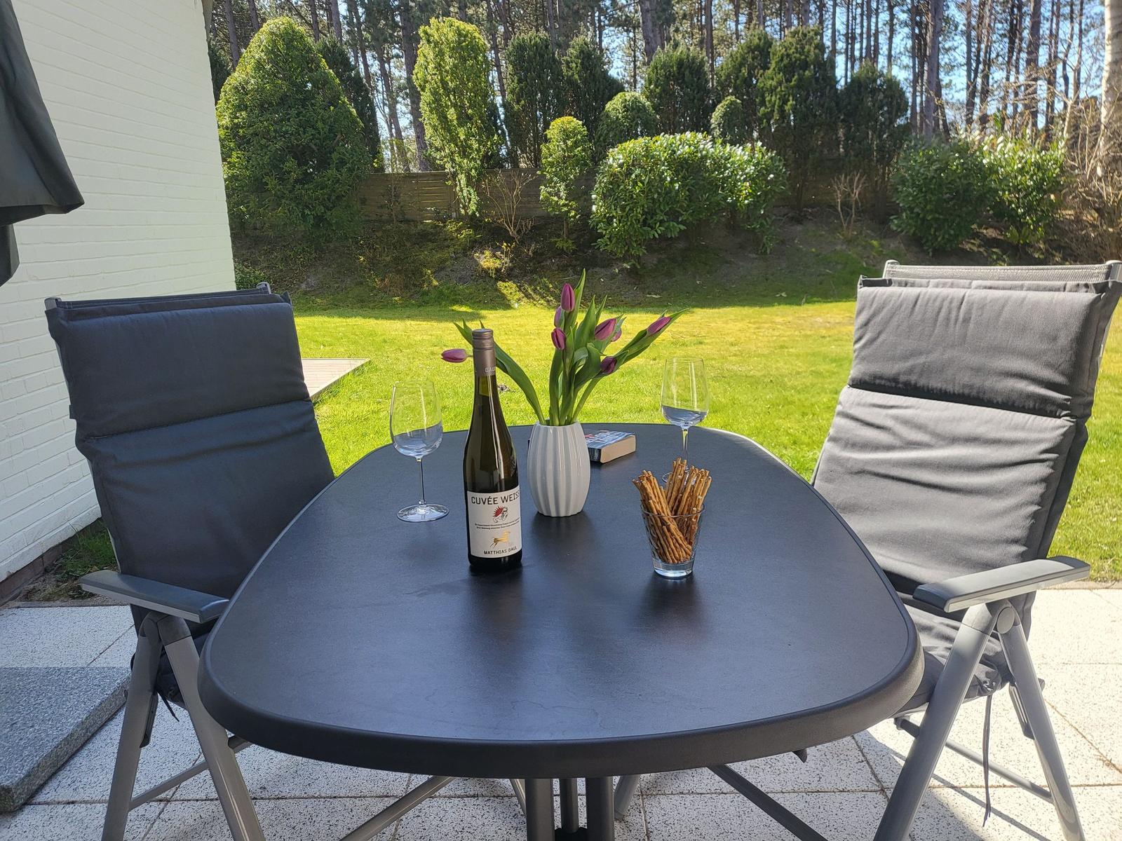 Außenbereich mit Tisch, zwei Stühlen, Wein, Tulpen und Gebäck.