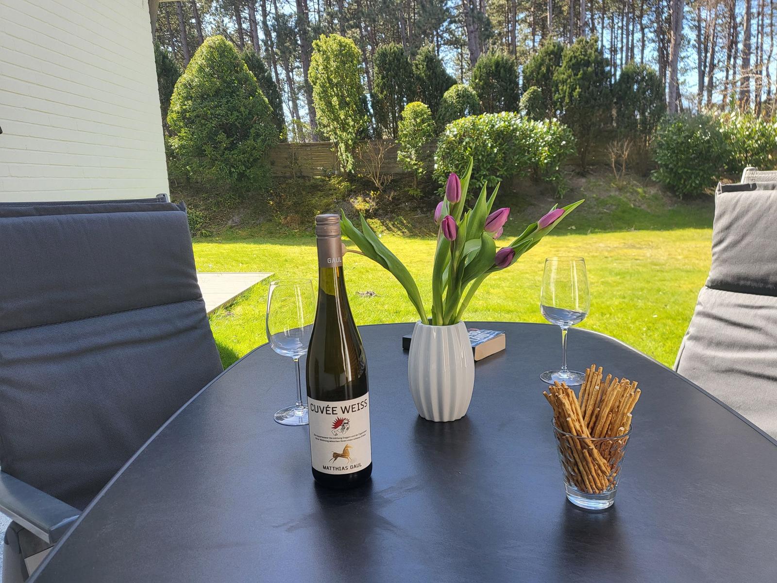 Tisch mit Wein, Tulpen und Knäckebrot auf Terrasse mit Gartenblick.