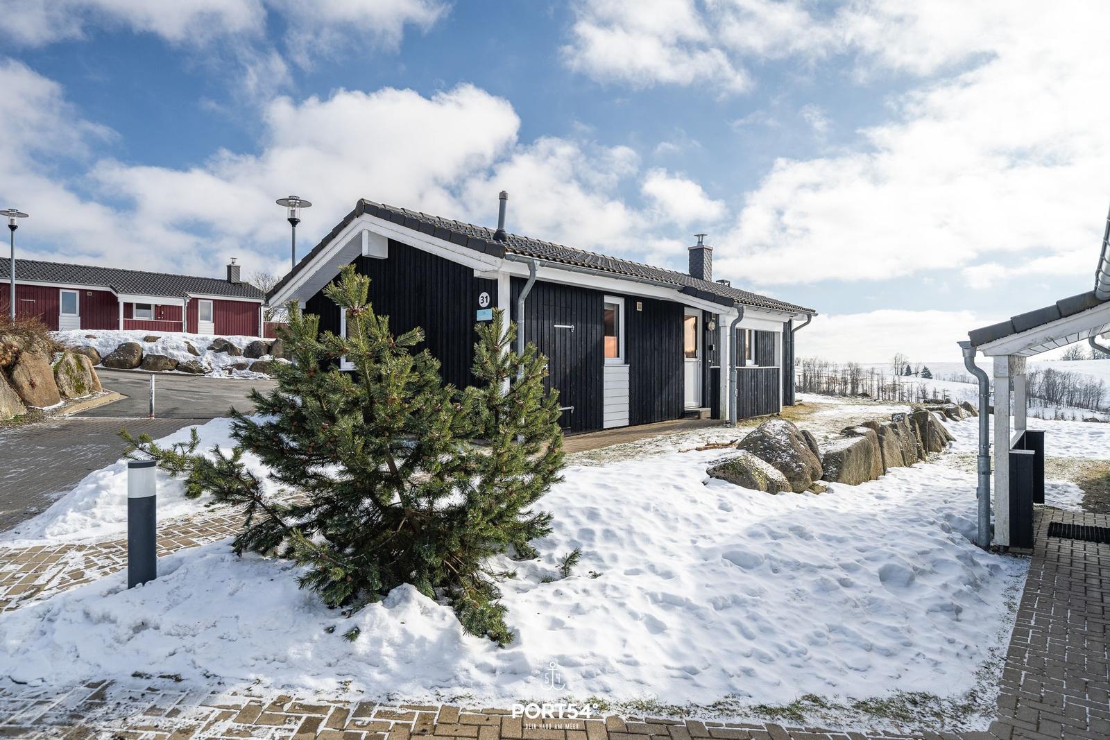 Schwarzes Holzhaus mit Schneebedecktem Vorgarten und Blick auf verschneite Landschaft.