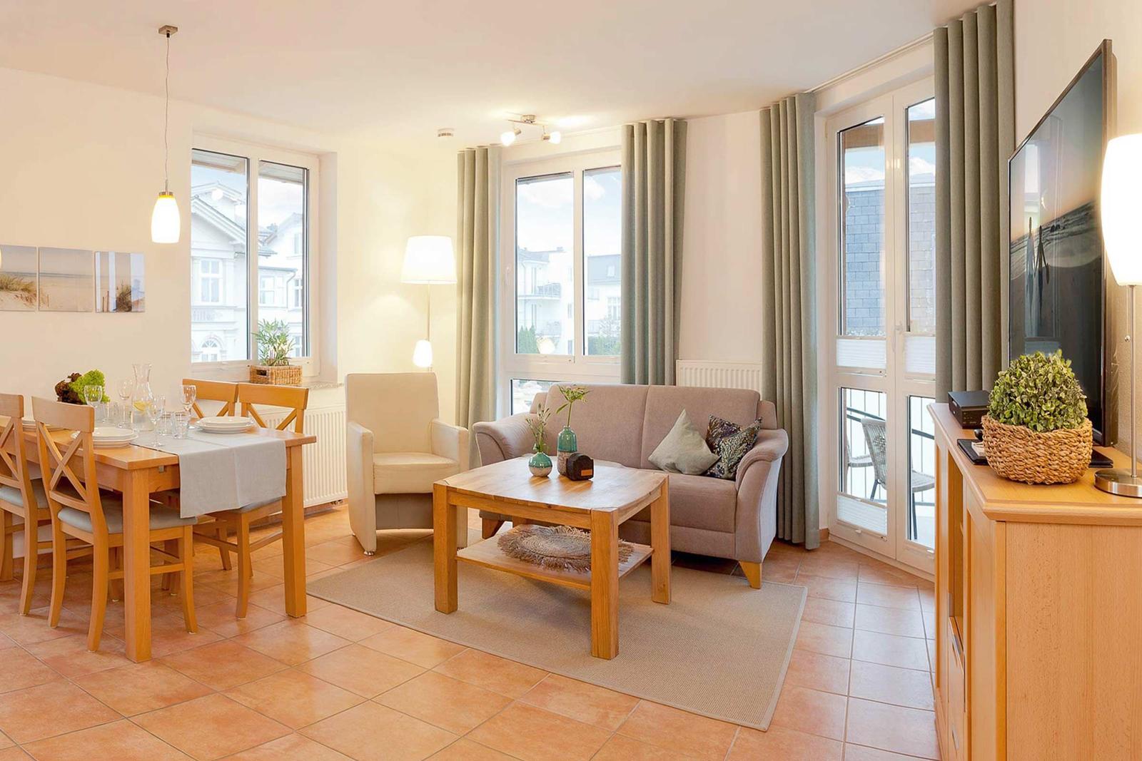 Wohn- und Essbereich mit Sofa, Esstisch und TV. Durchgänge zu Balkon.