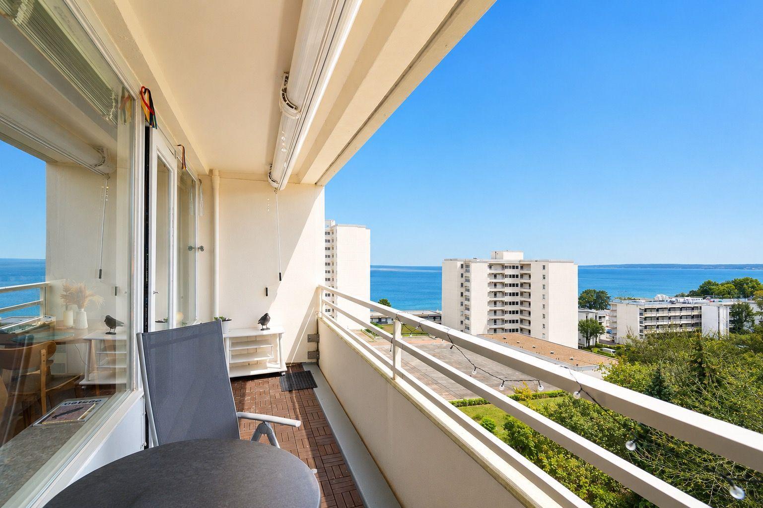 Balcony with seating and view of the sea and high-rise buildings.