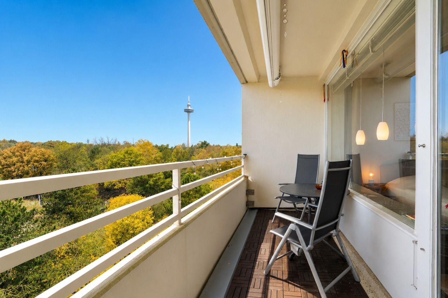 Balcony with table and chairs, view of forest and tower.