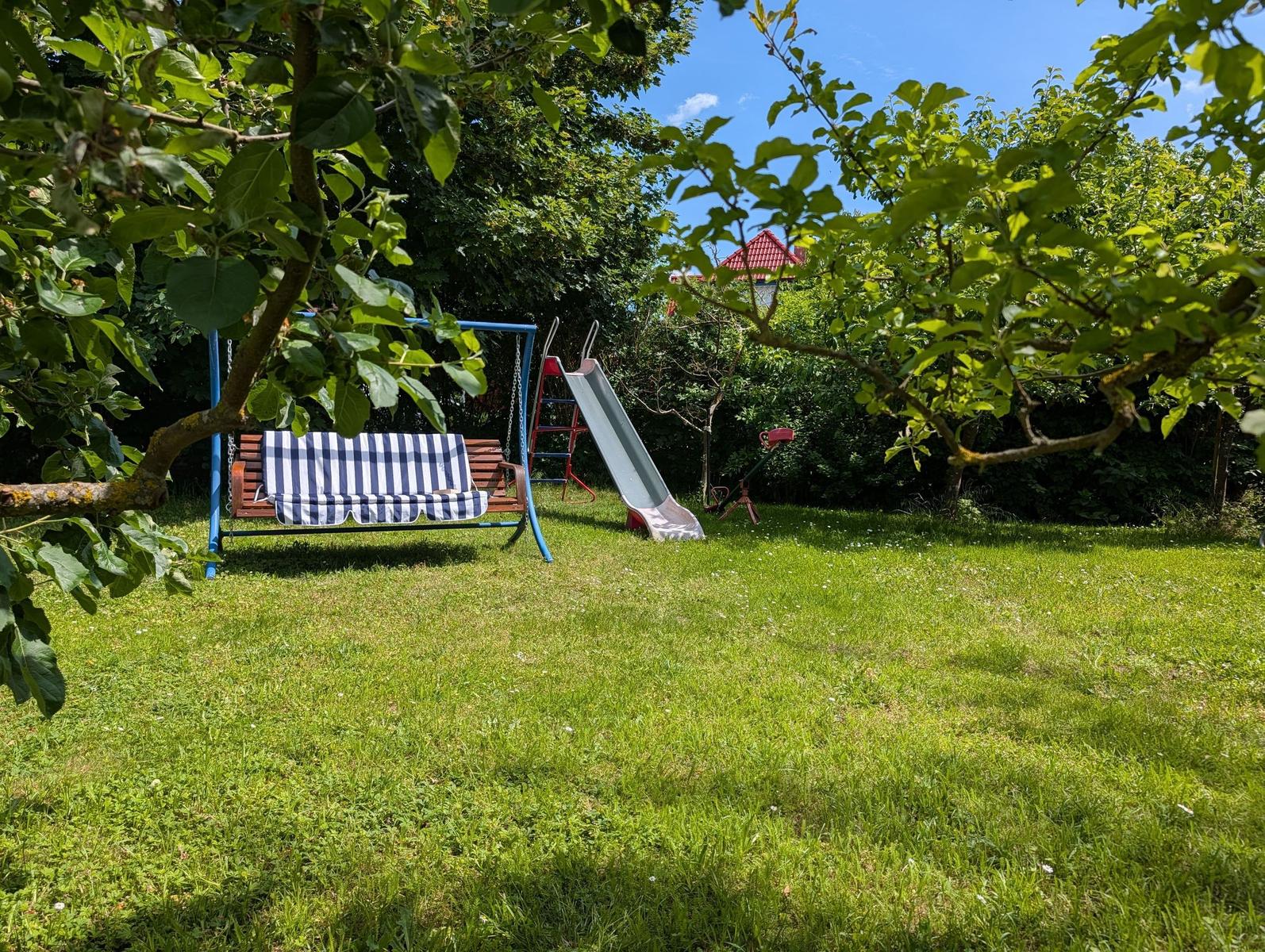 Hinterhof mit Schaukel, Rutsche und Spielplatz unter Bäumen.