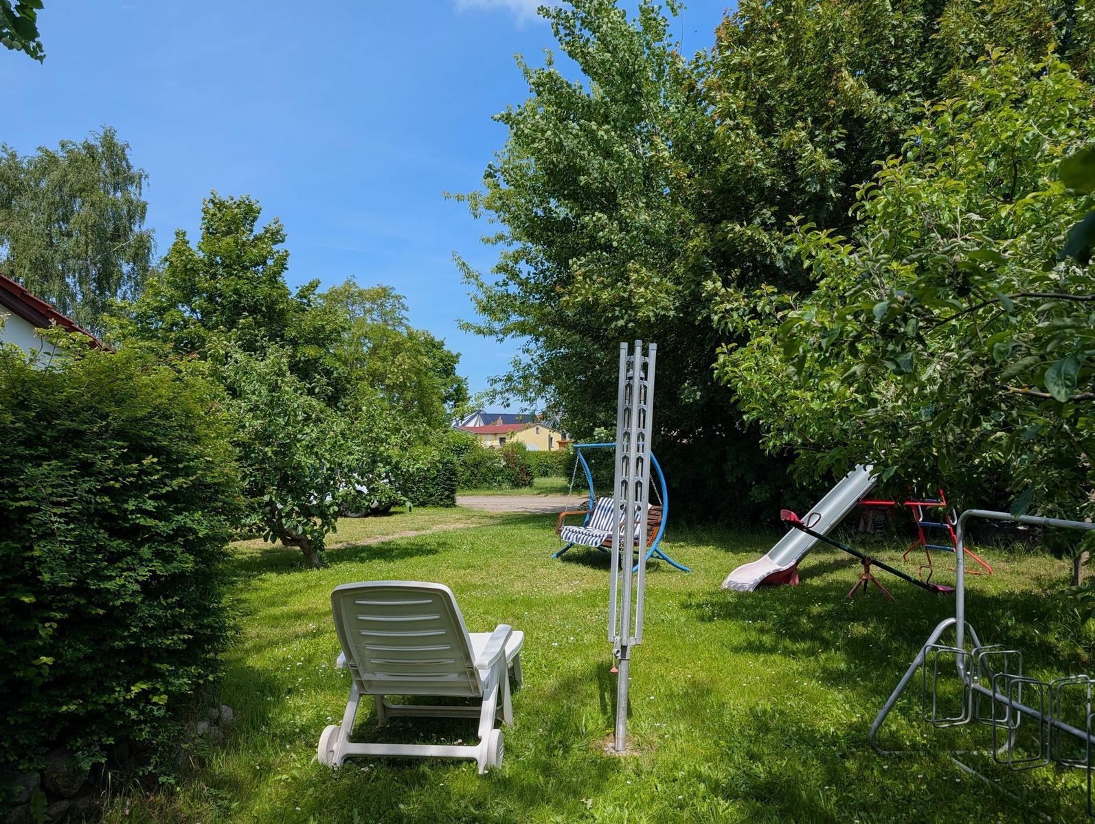 Hinterhof mit Liegestuhl, Schaukel und Rutsche unter Bäumen.