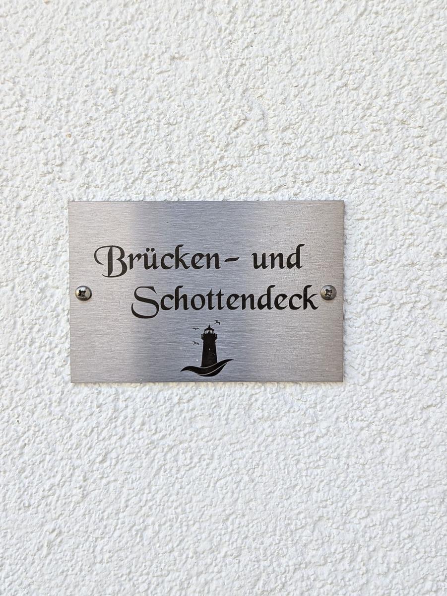 Metalltafel mit Schriftzug und Leuchtturm-Symbol an weißer Wand