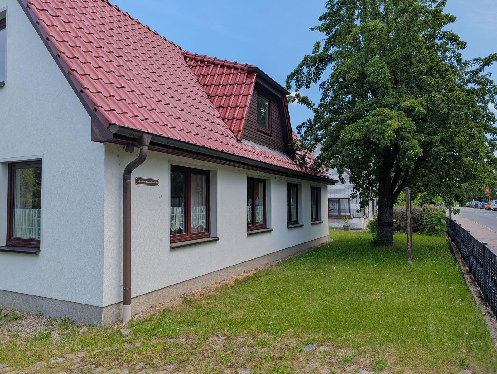 Ein Haus mit rotem Dach und weißen Wänden, umgeben von Gras und Bäumen.