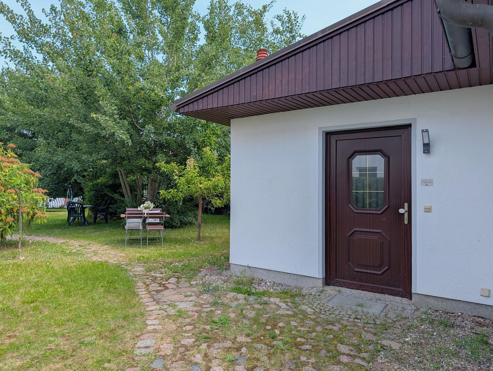 Haus mit brauner Tür und Steinweg im Garten mit Tisch und Stühlen.
